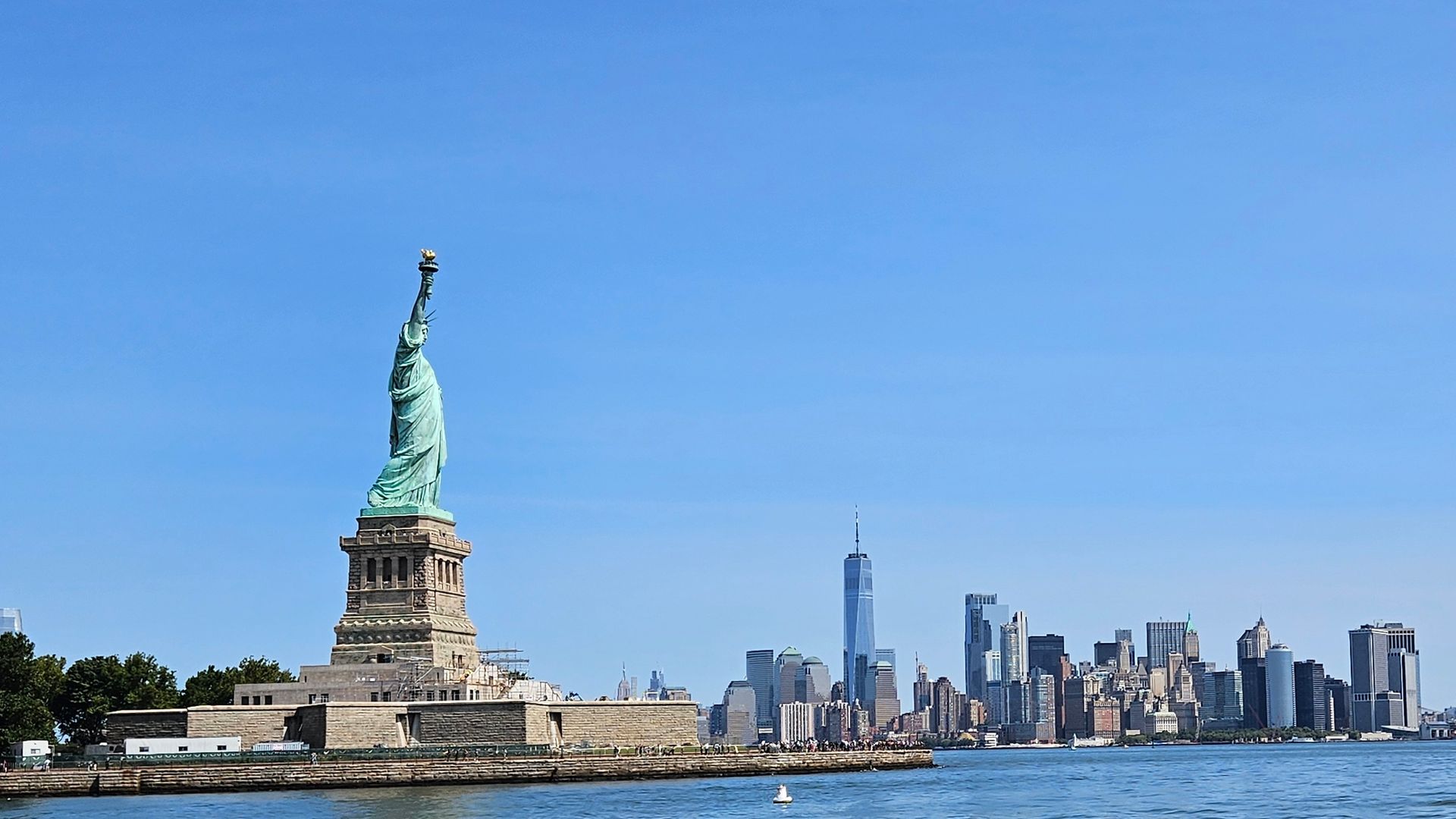 Statue of Liberty with NYC skyline in the background, under a clear blue sky.