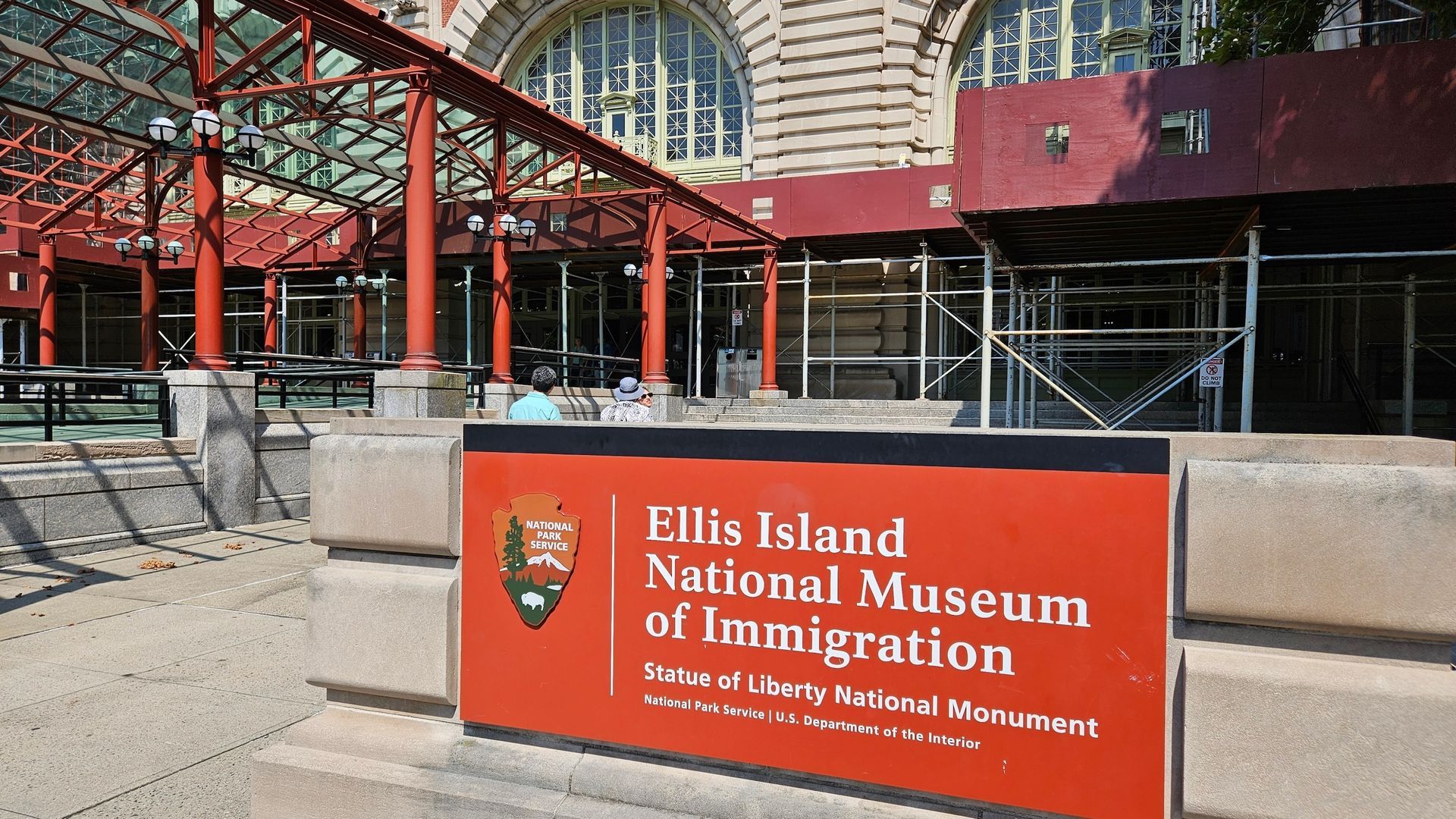 Ellis Island National Museum of Immigration exterior, red sign, building with arched windows, metal framework, New York City.