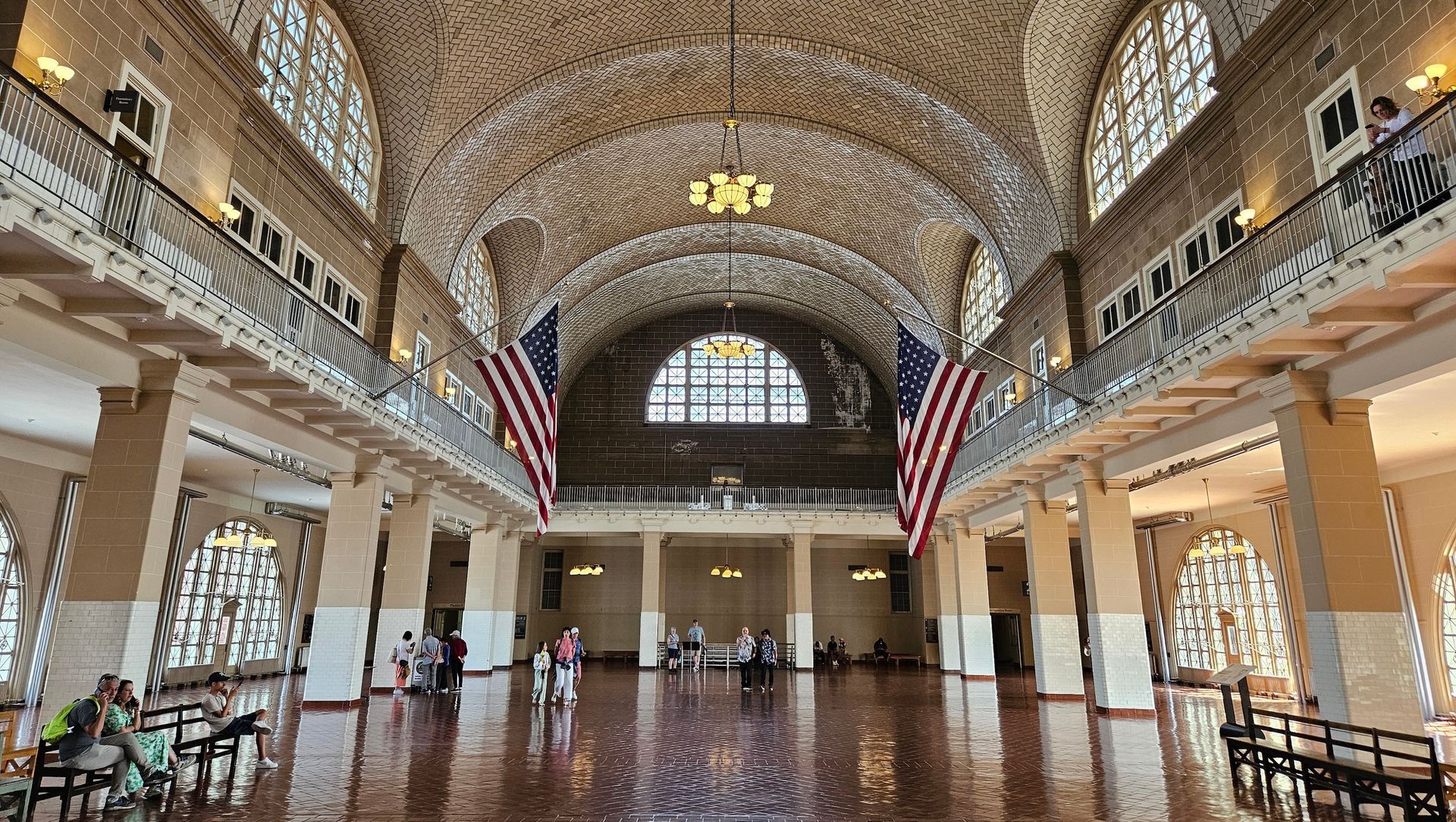 Ellis Island's Great Hall with arched ceiling, American flags, and a few people standing.