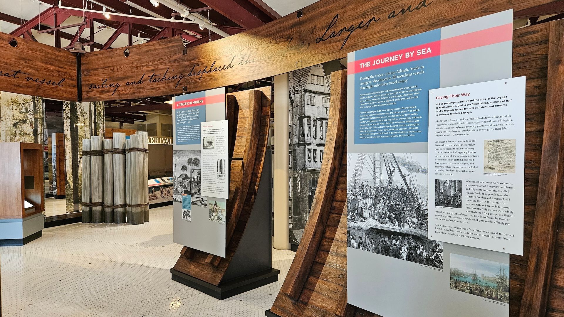 Museum exhibit: displays with text and images about history, wooden beams overhead, indoor setting.