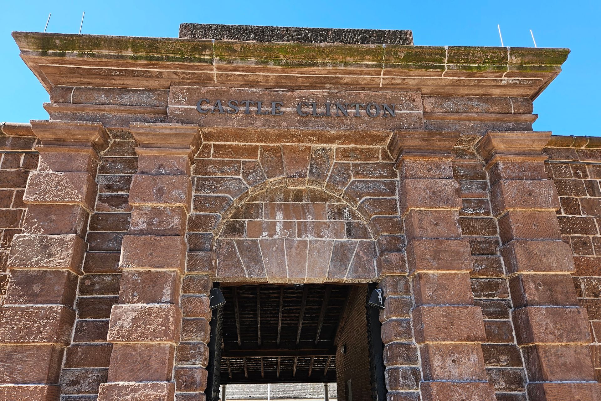 Stone archway entrance, brown brick structure, weathered, blue sky background.