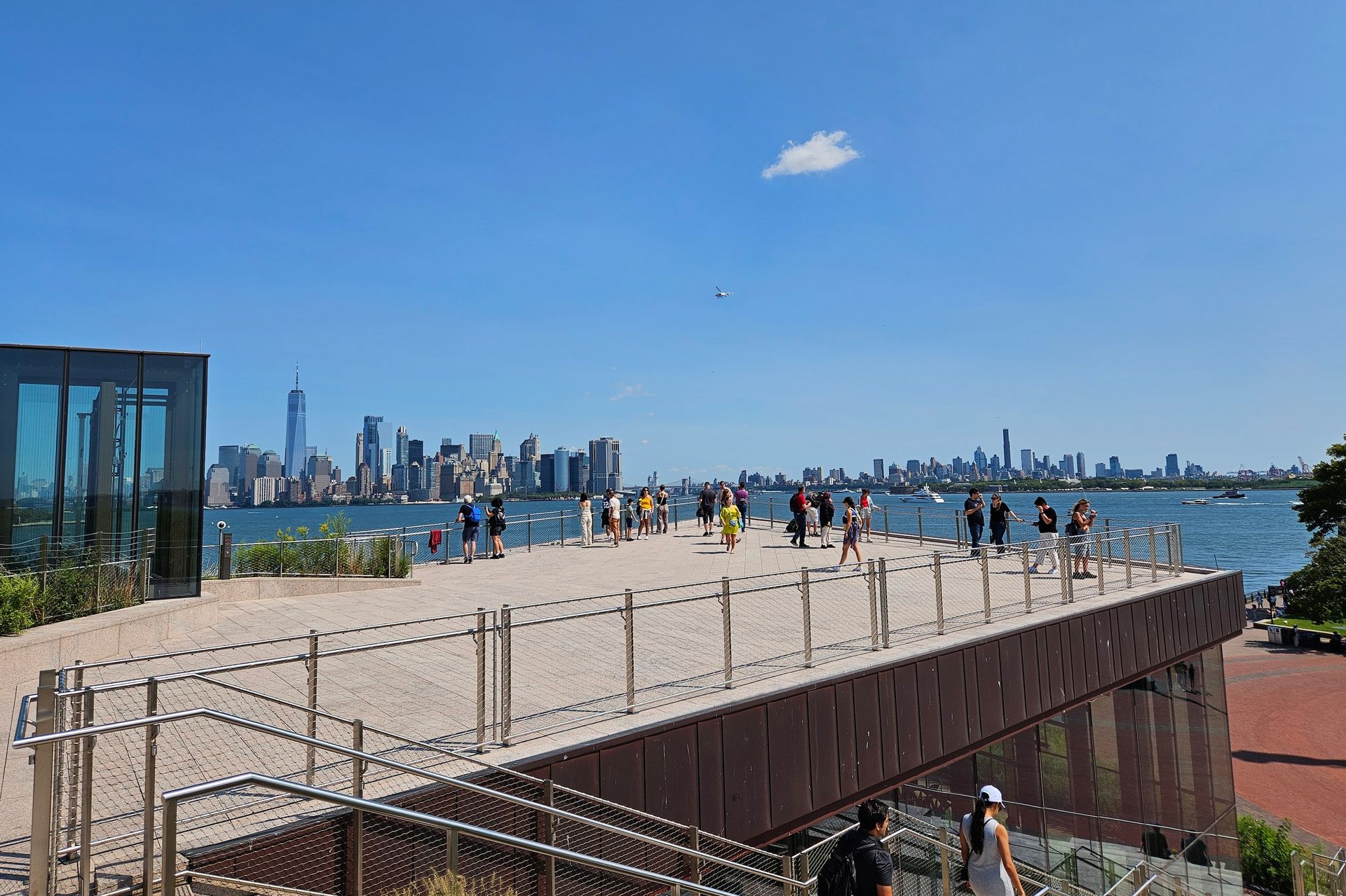 People on a viewing platform overlooking NYC skyline on a sunny day.