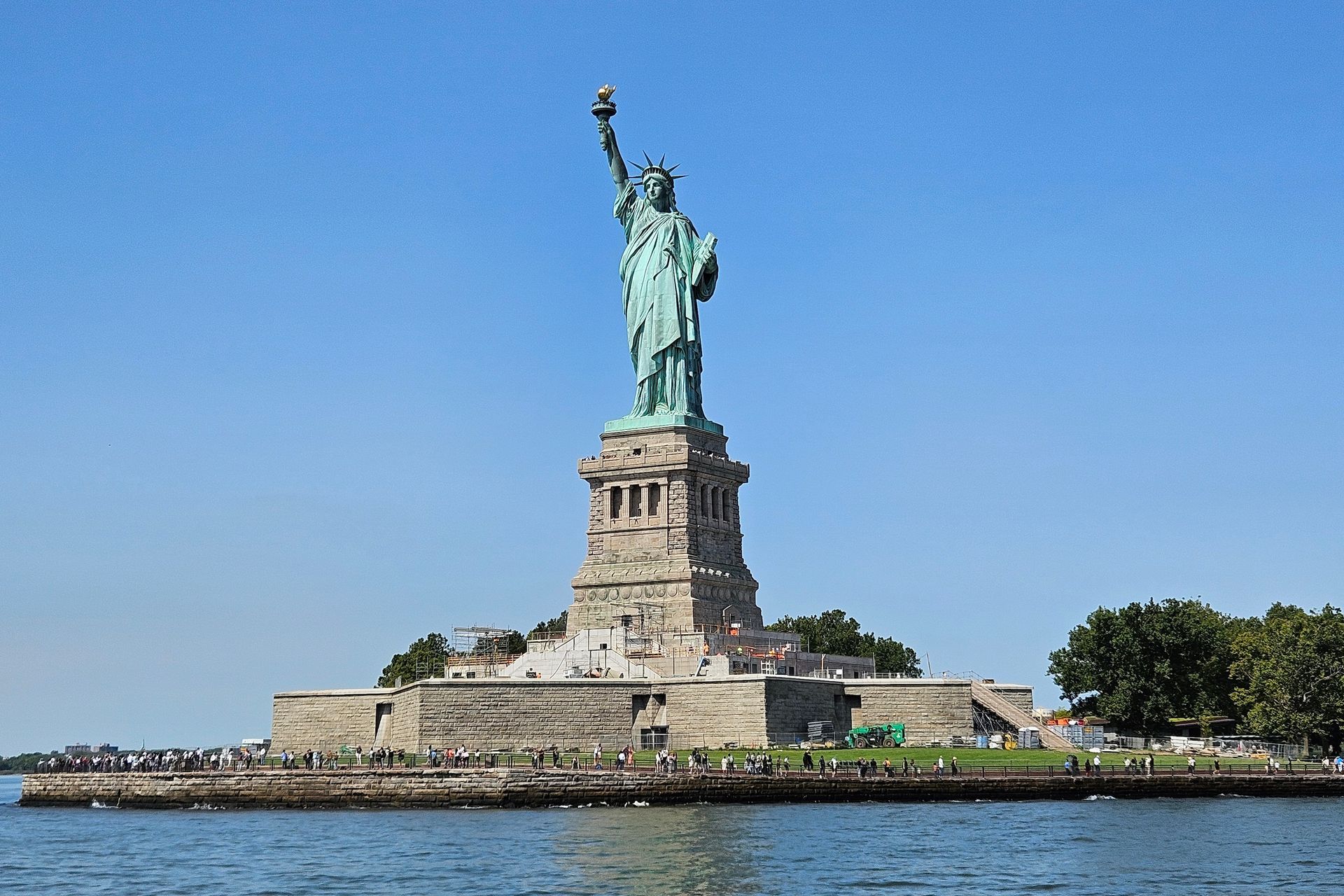 Statue of Liberty stands tall on Liberty Island with a blue sky and water.