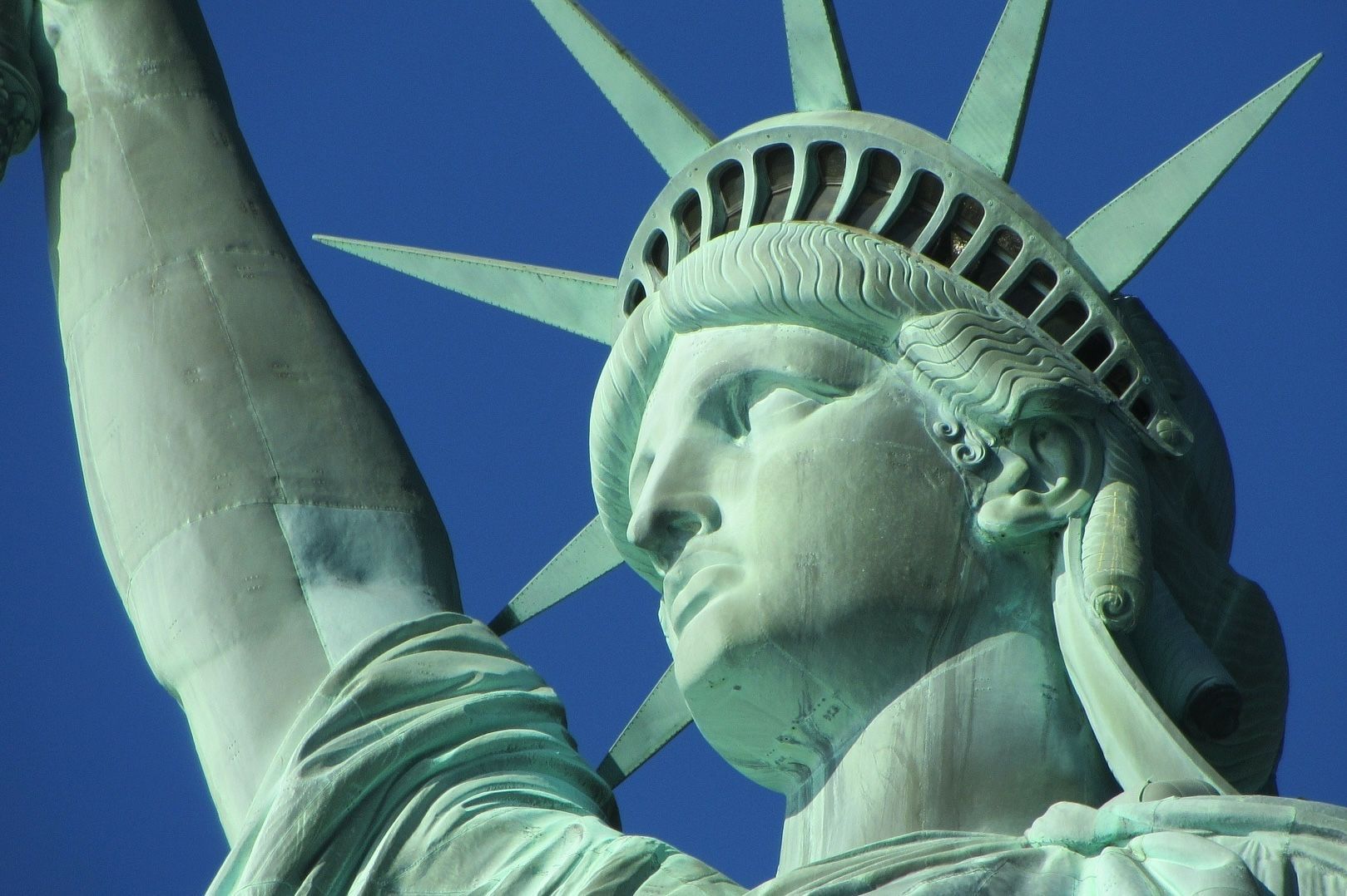 Statue of Liberty against a clear blue sky; copper-green statue with sun-like crown.