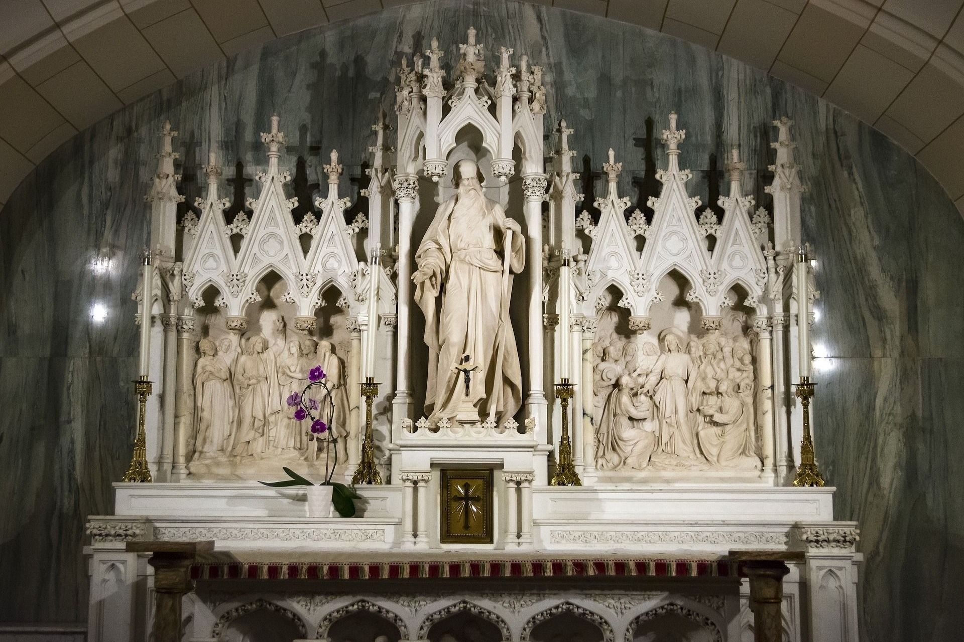 Altar with statue of a robed figure flanked by sculptures in a church. Green marble background.