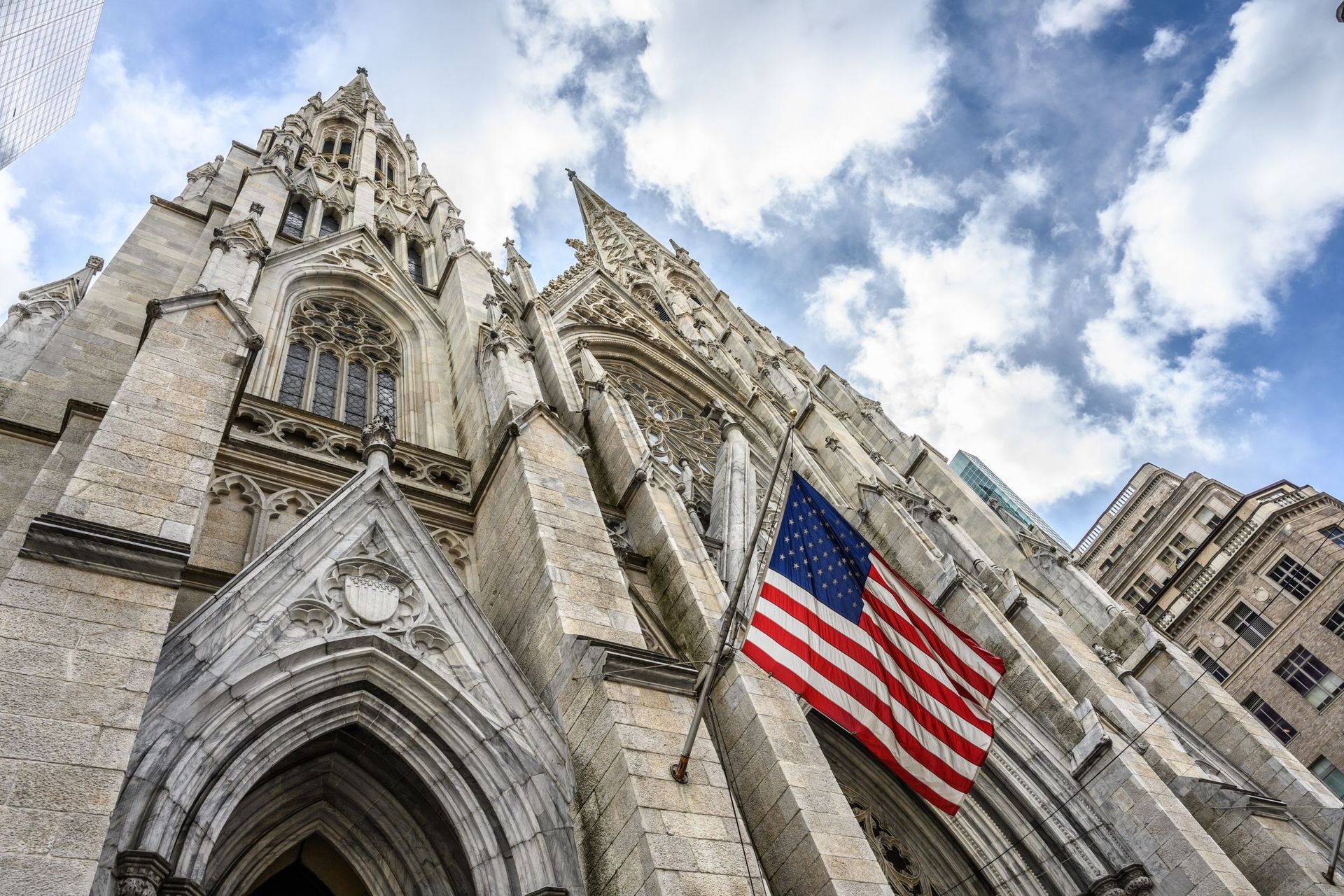 Exterior of St. Patrick's Cathedral in New York City, with the American flag hanging; bright sky.