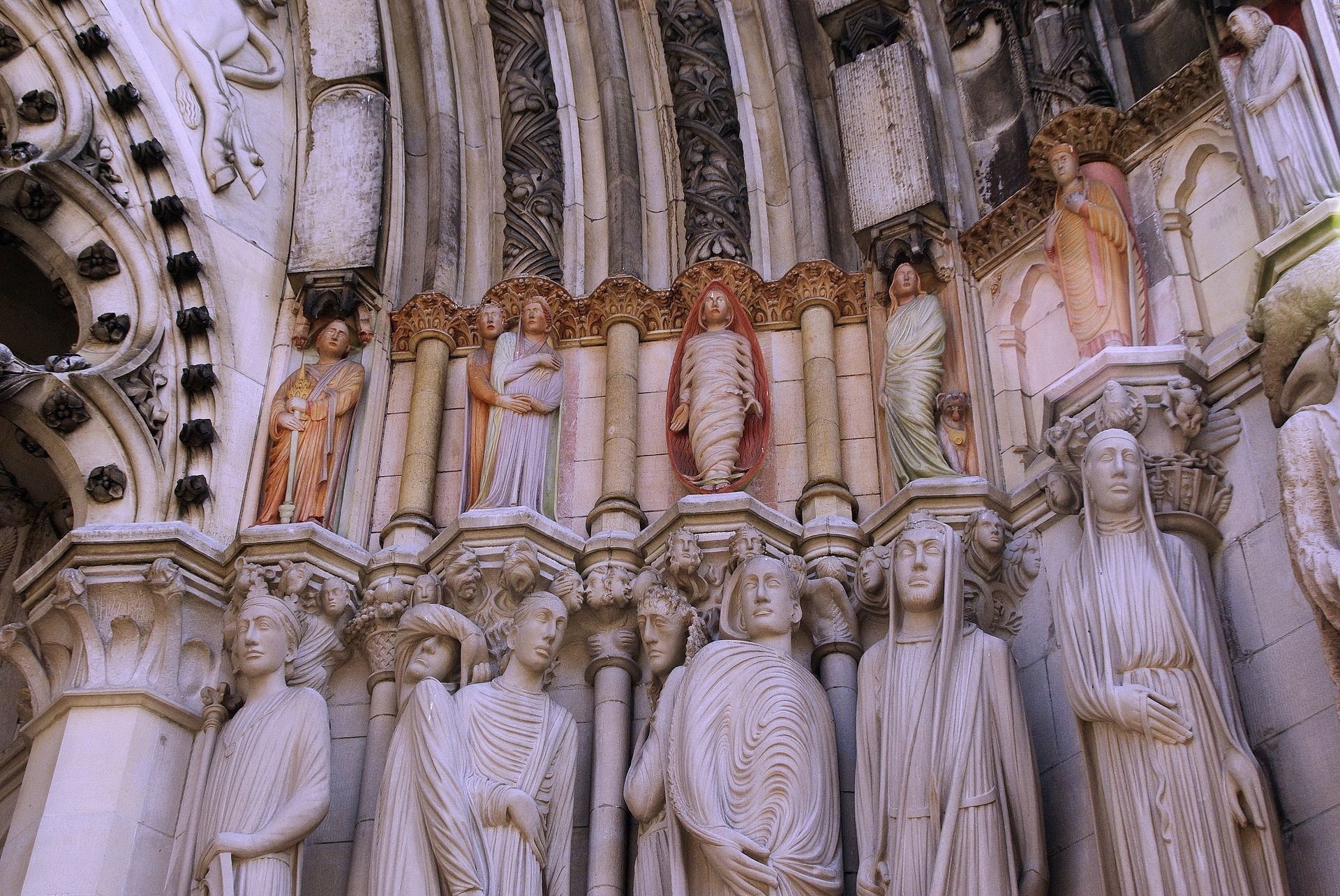 Statues of religious figures on a cathedral entrance, some with painted detail, in various poses.