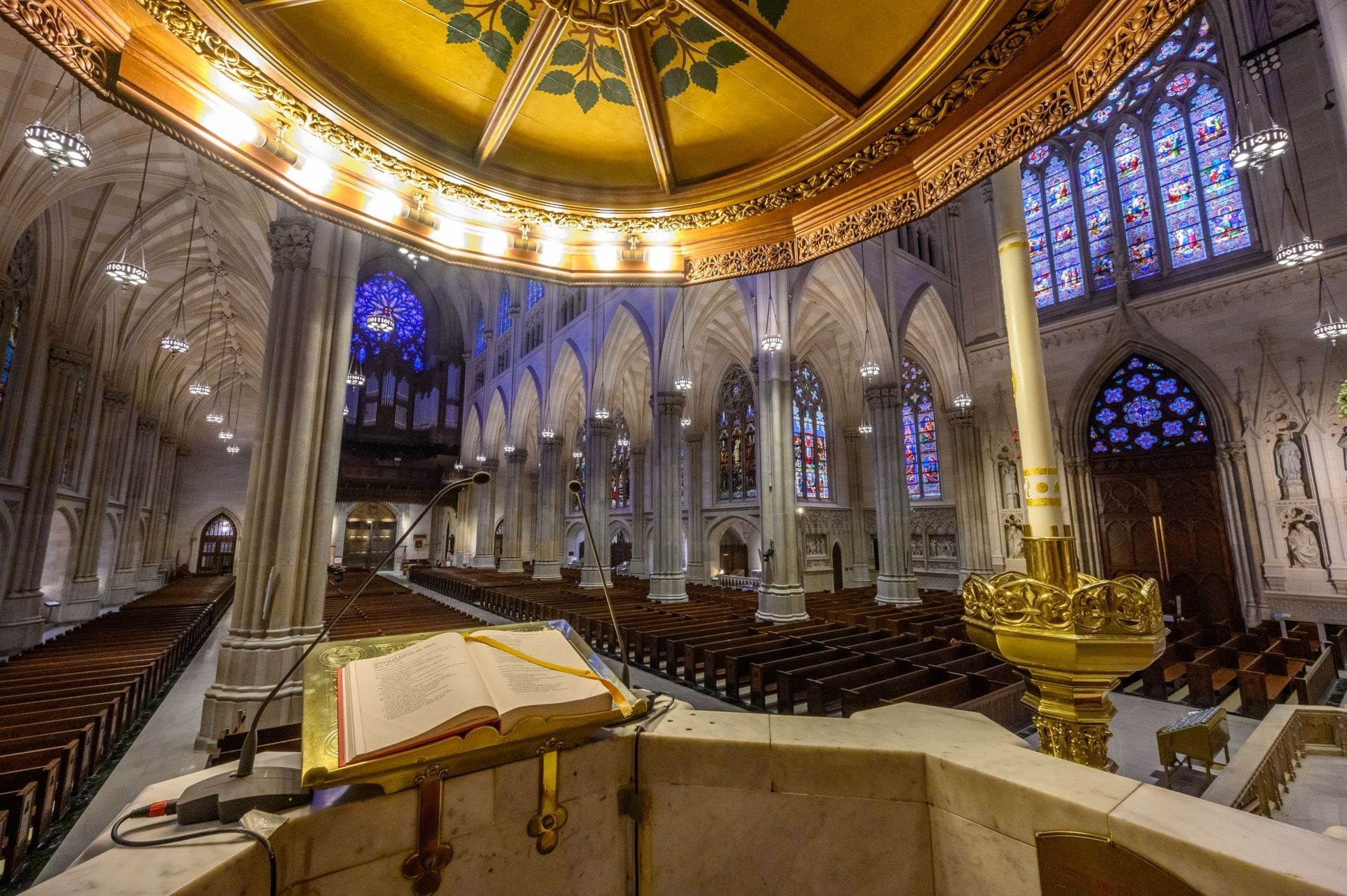 Interior of a cathedral with high arches, stained glass windows, and pews.