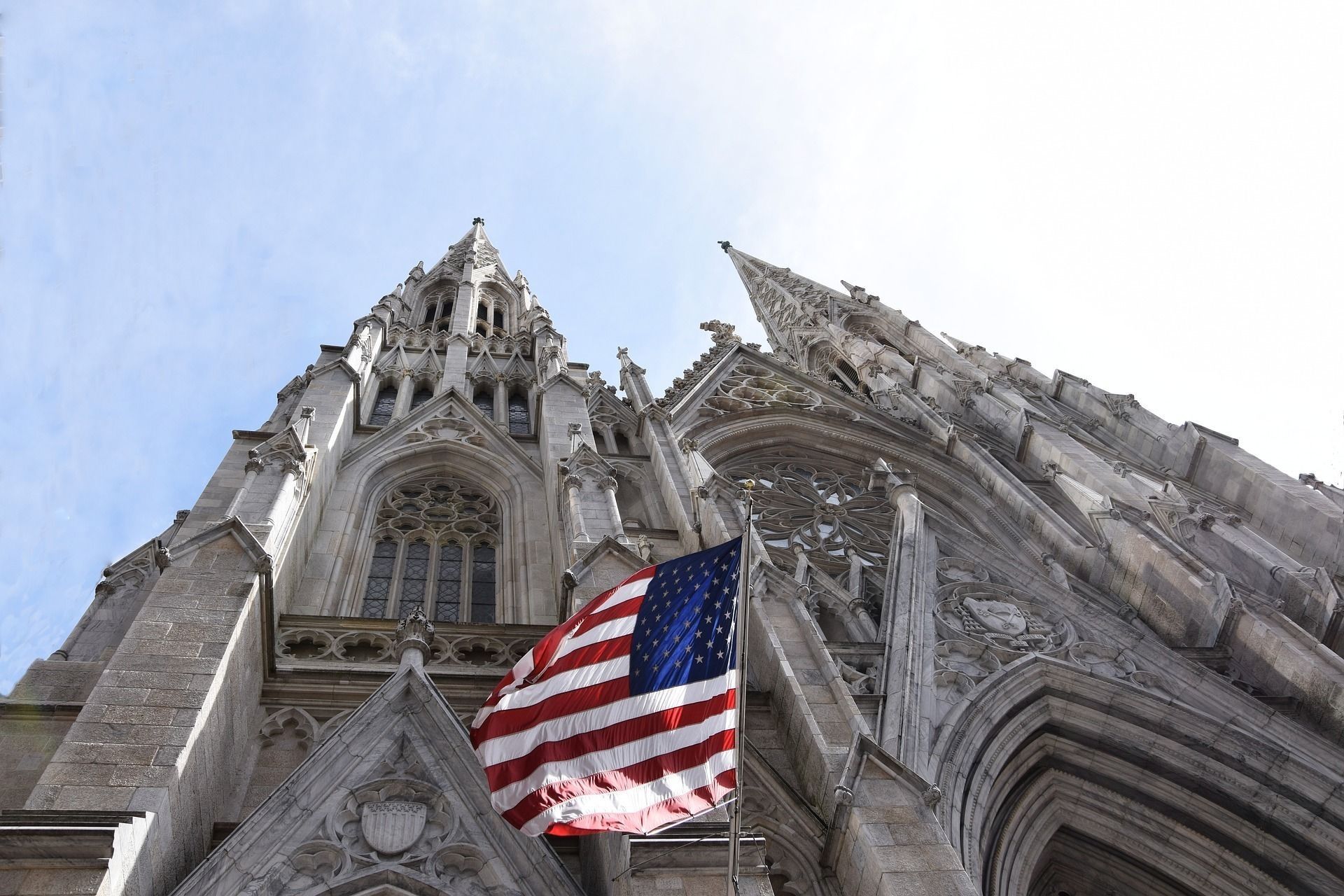 American flag flies from the side of a stone cathedral under a bright blue sky.