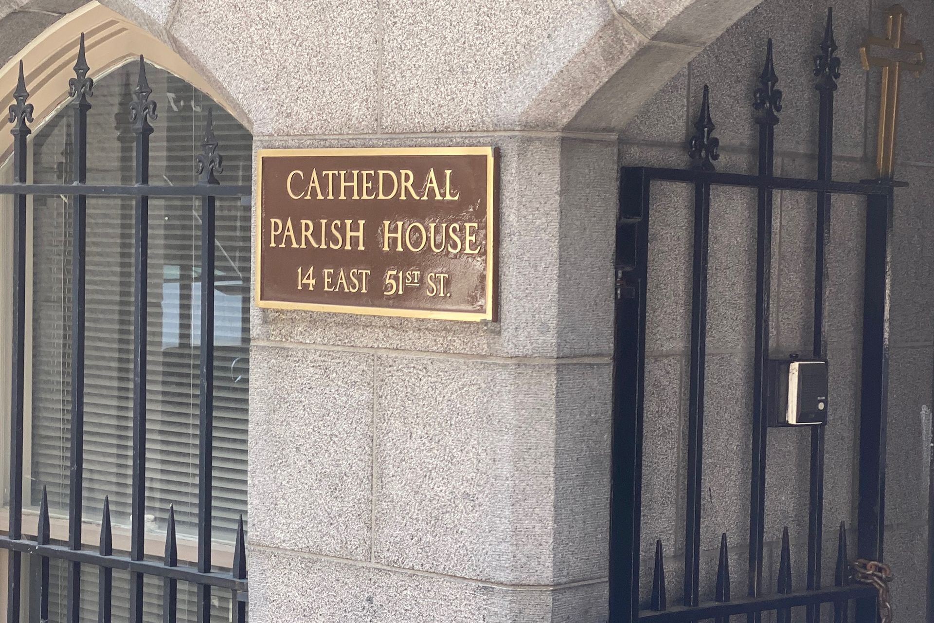 Sign for Cathedral Parish House at 64 East 9th Street on a stone wall with a black gate and barred window.
