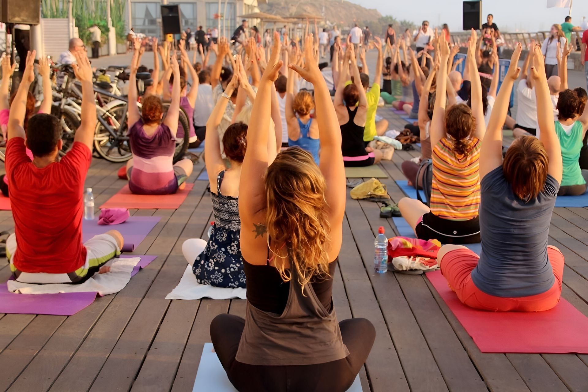 People doing yoga on a wooden deck near the ocean with arms raised.