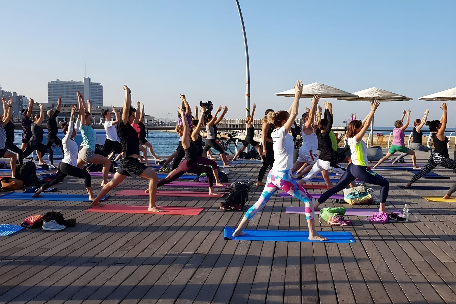 Yoga class on a pier with many people in warrior pose; blue sea, sky.