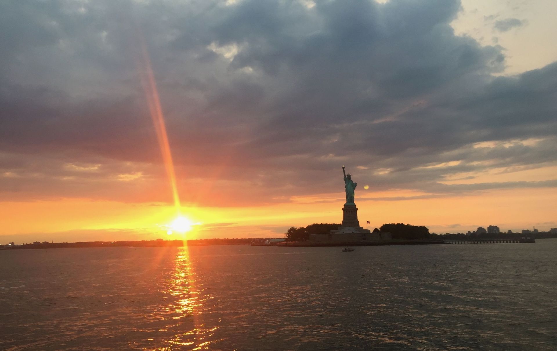 Statue of Liberty silhouetted against a fiery sunset over the water in New York.