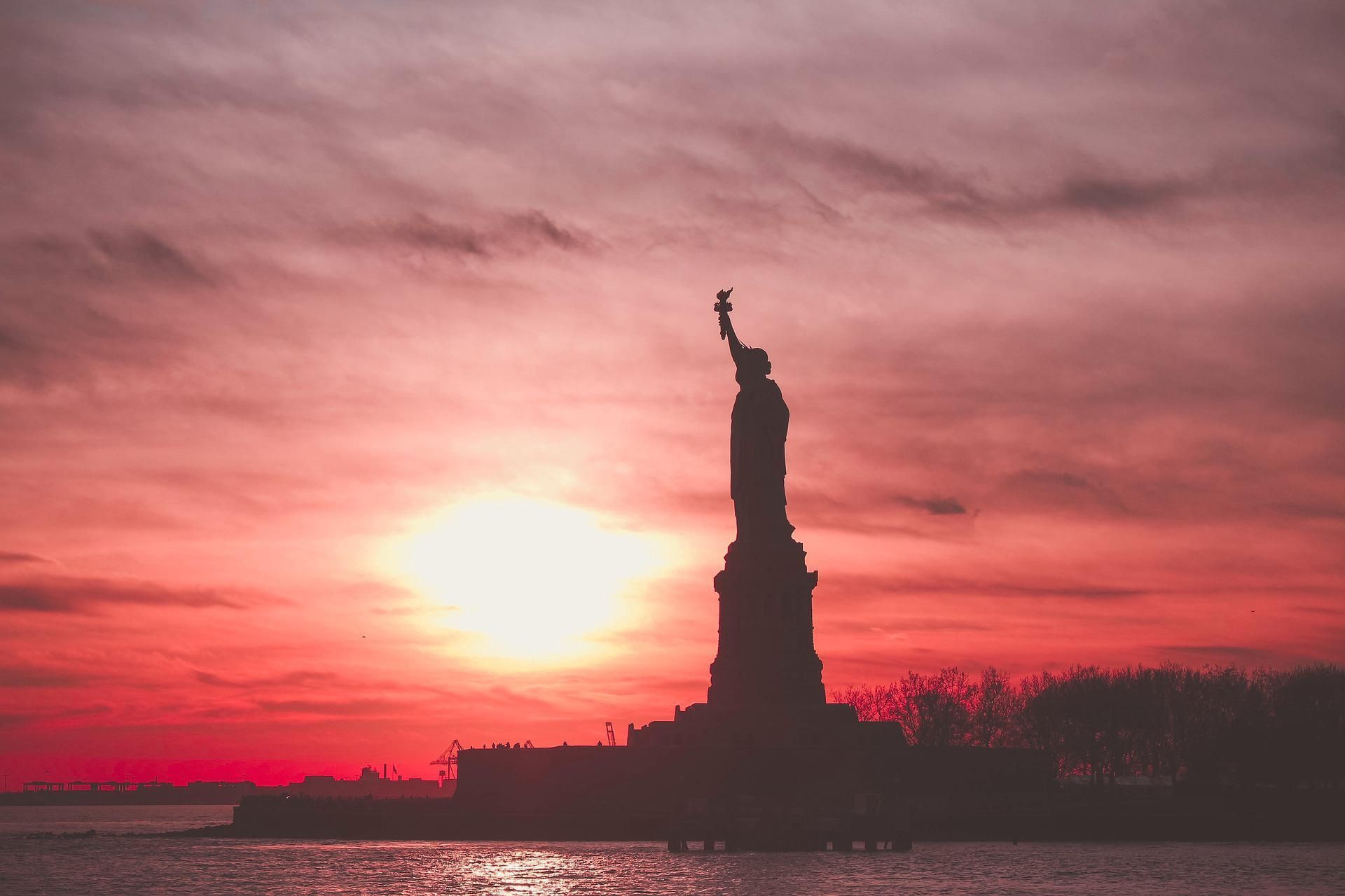 Statue of Liberty silhouetted against a vibrant red sunset over water.