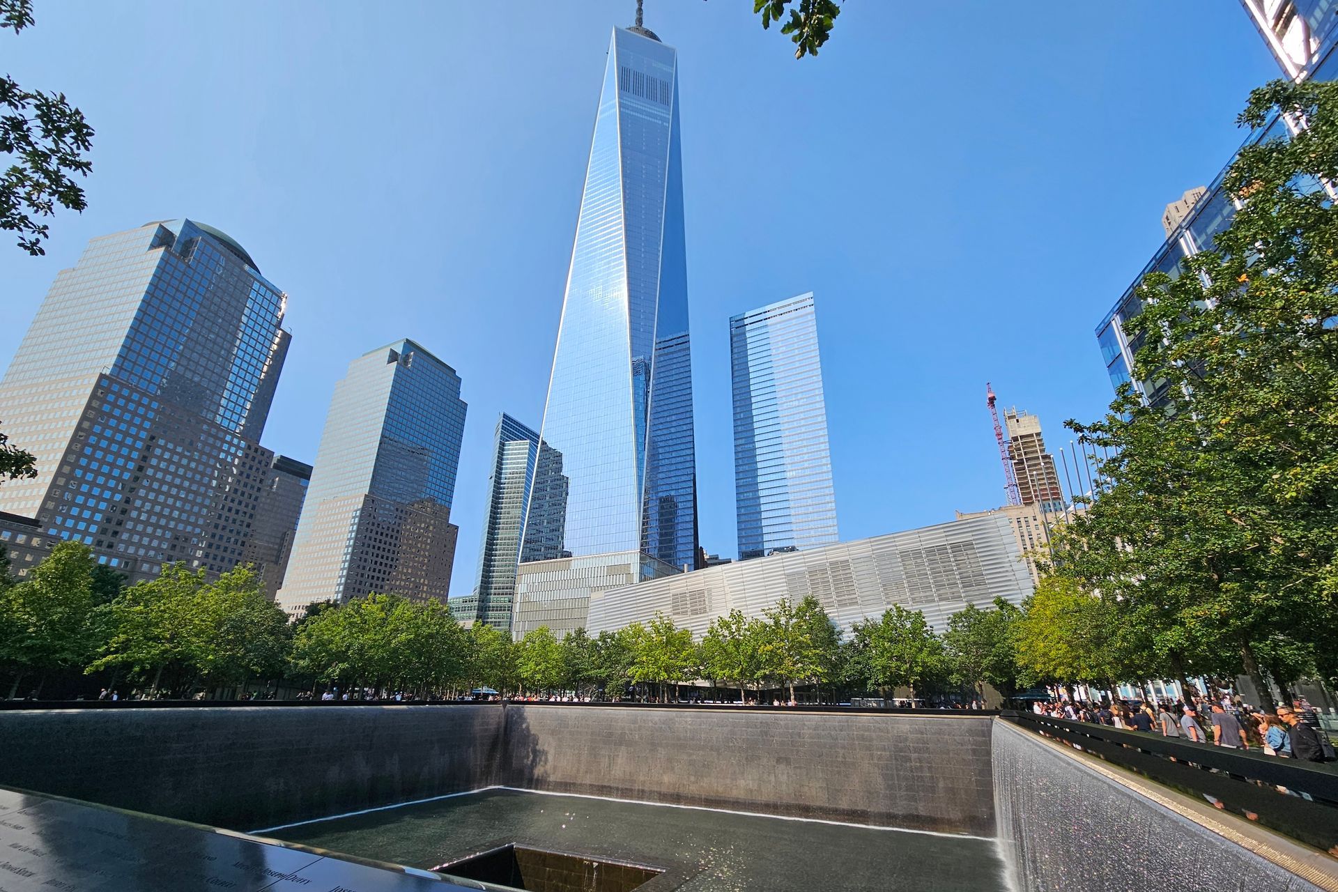 One World Trade Center, 9/11 Memorial with reflecting pools, blue sky, and other skyscrapers.