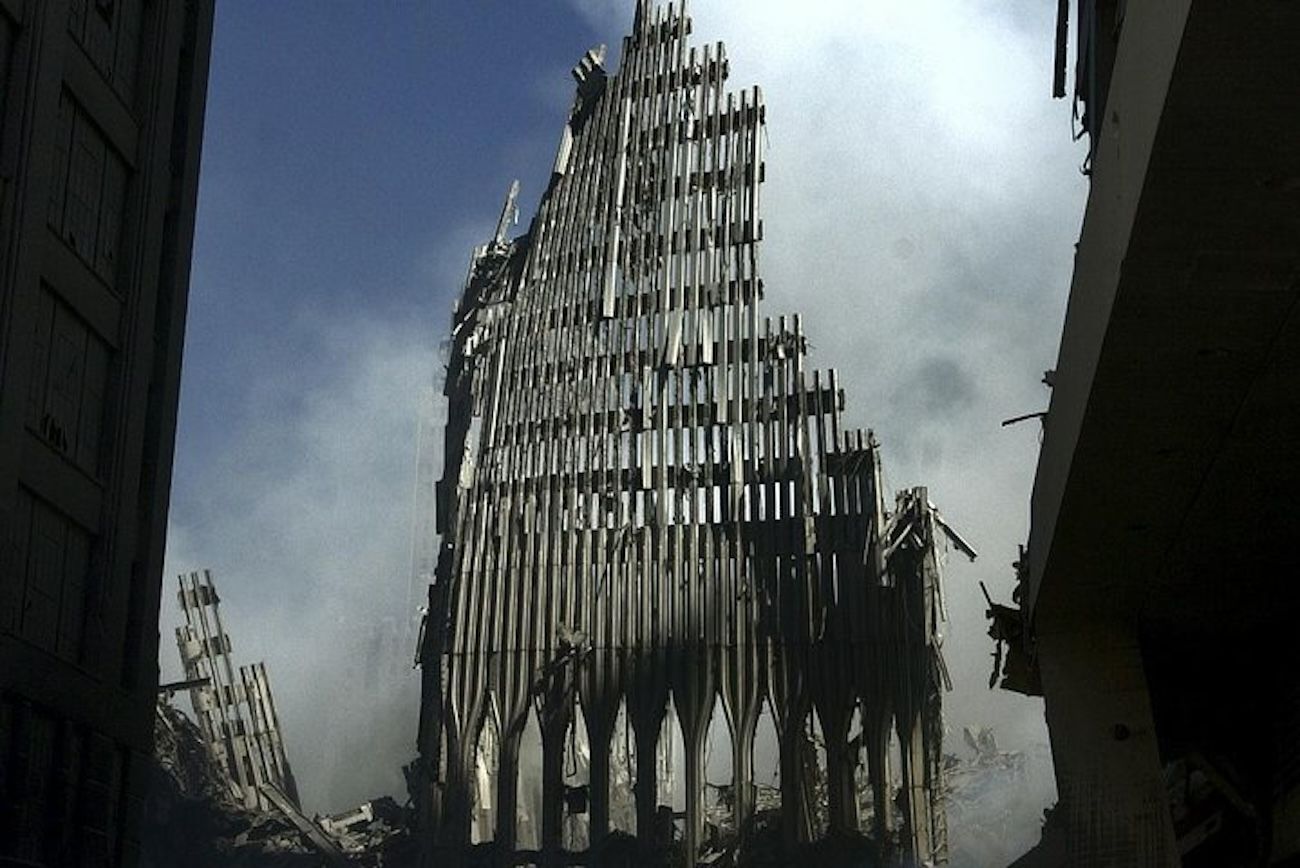Remnants of the World Trade Center after the 9/11 attacks, revealing a skeleton of the towers against a smoky sky.