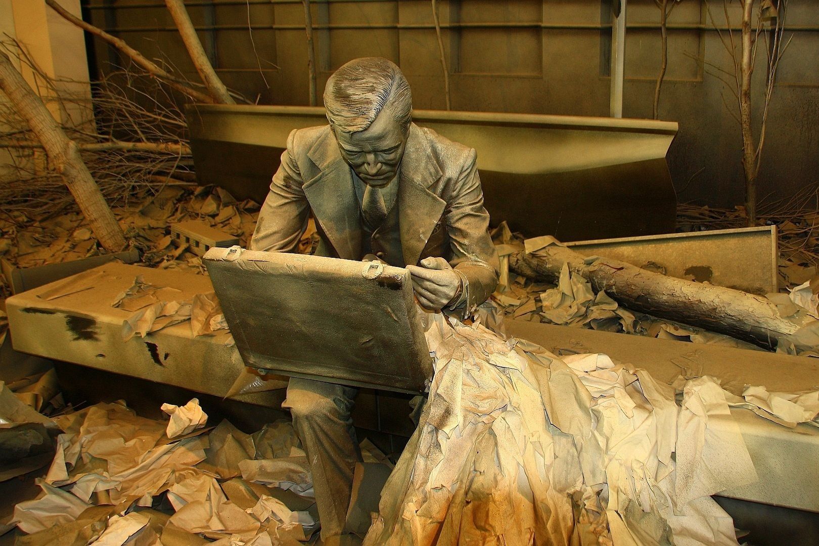 Bronze statue of a man seated, working on a case, with a boat and debris in the background.
