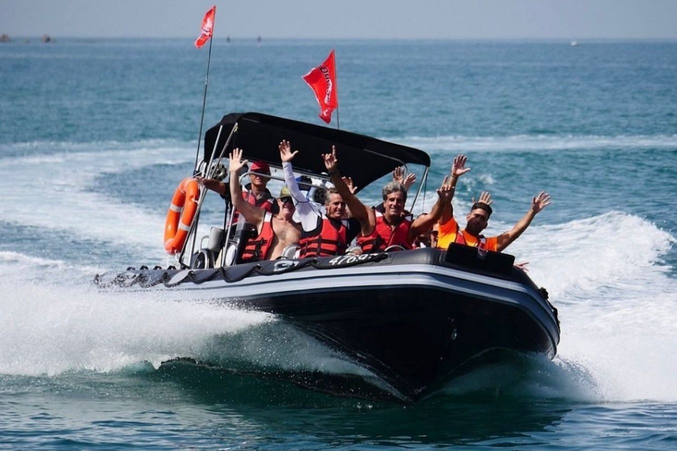 People on a black motorboat wave with excitement on a sunny day at sea.