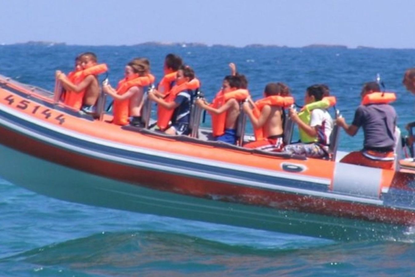 Children in orange life vests on an orange boat at sea.