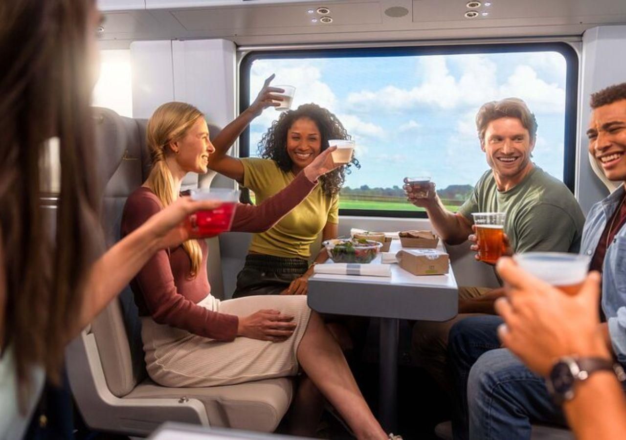 Group of friends on a train, toasting drinks, laughing. Light streaming through window, showing green landscape.