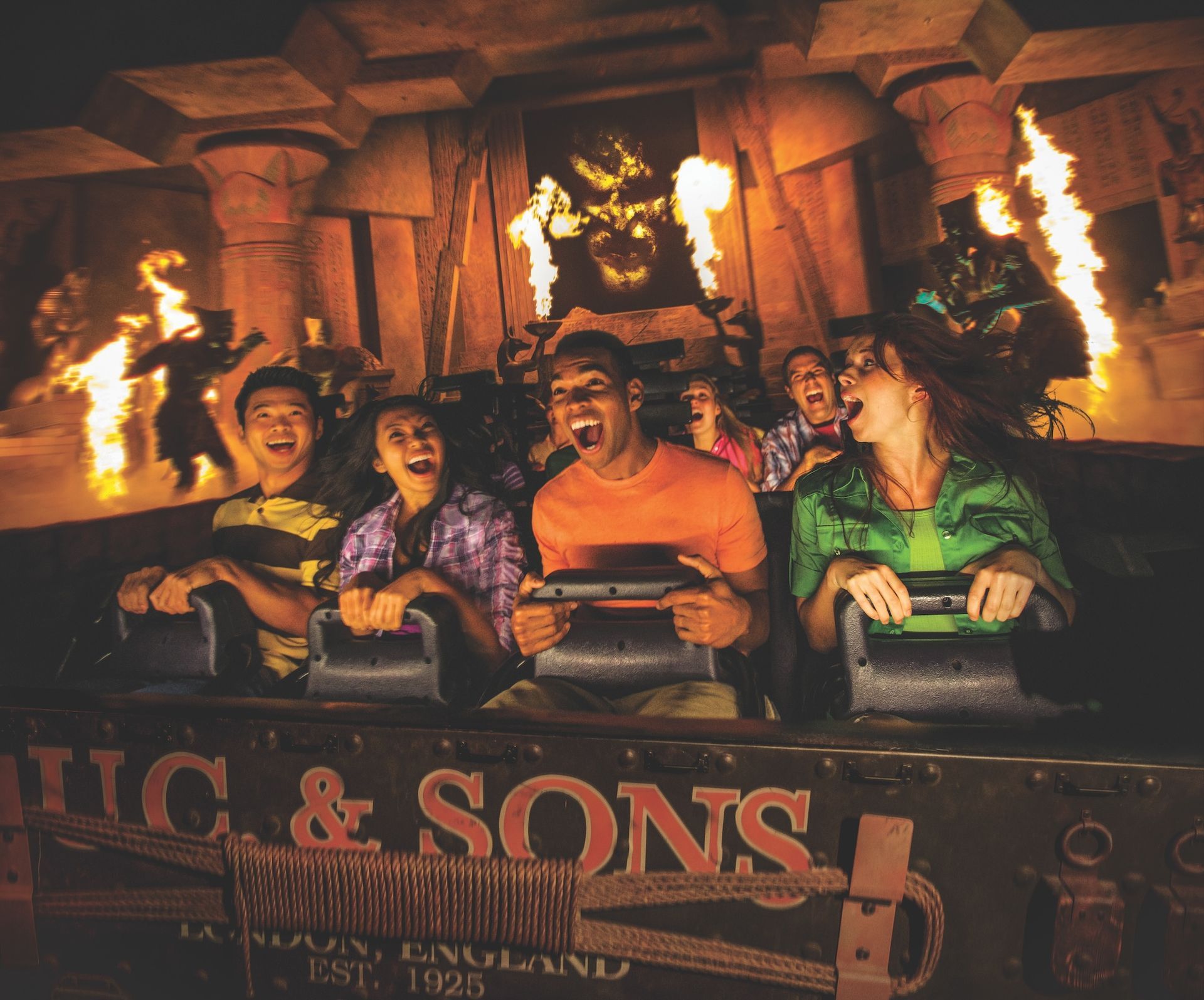 People on a roller coaster, illuminated by fire and a demonic figure in a temple.