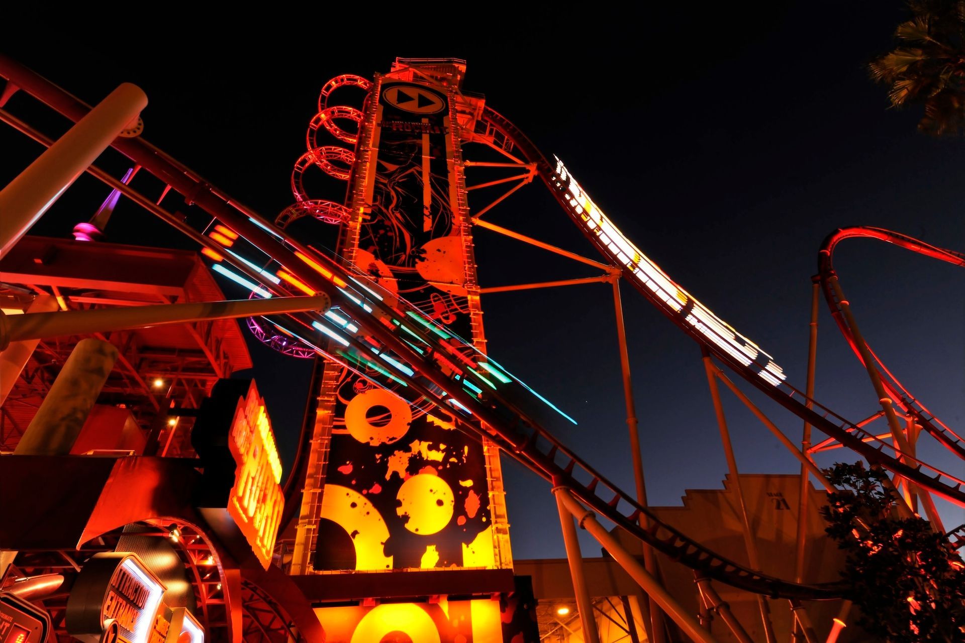Rollercoaster at night, lit in orange and yellow, with a tall tower structure.