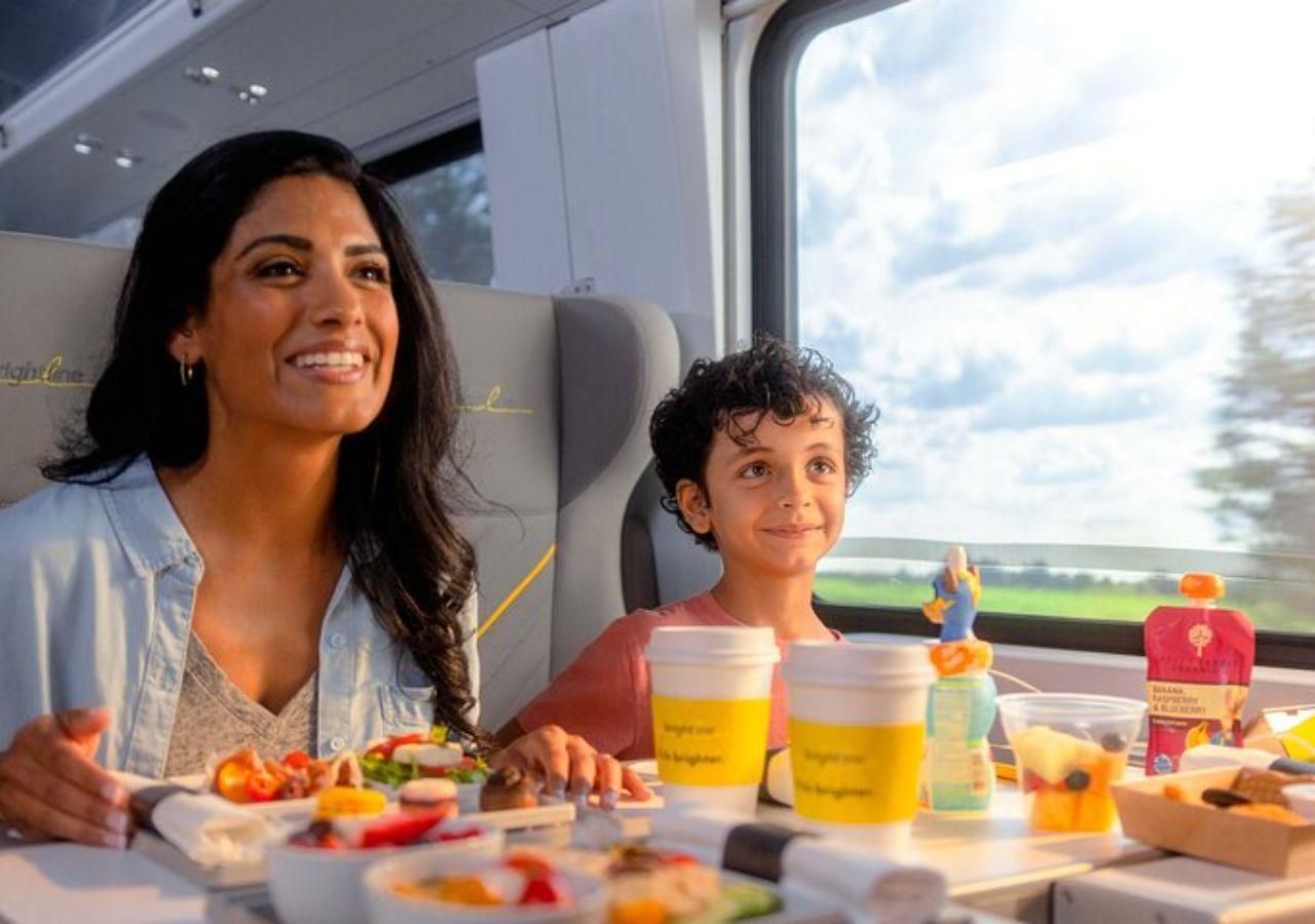 Woman and boy smiling, enjoying meal on train. Scenic outside view.