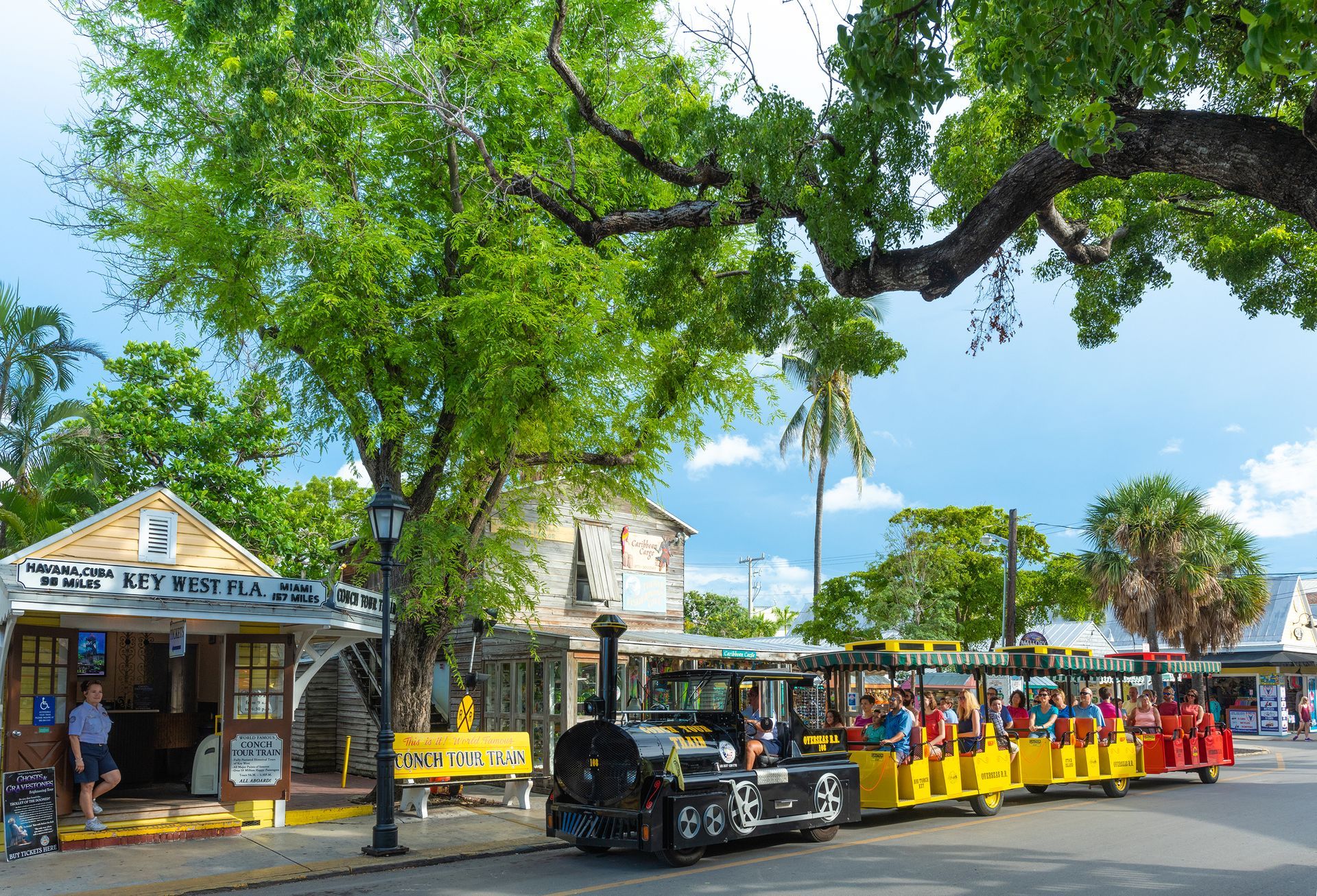 A yellow Conch Tour Train in Key West, Florida, with passengers and a ticket booth in view.