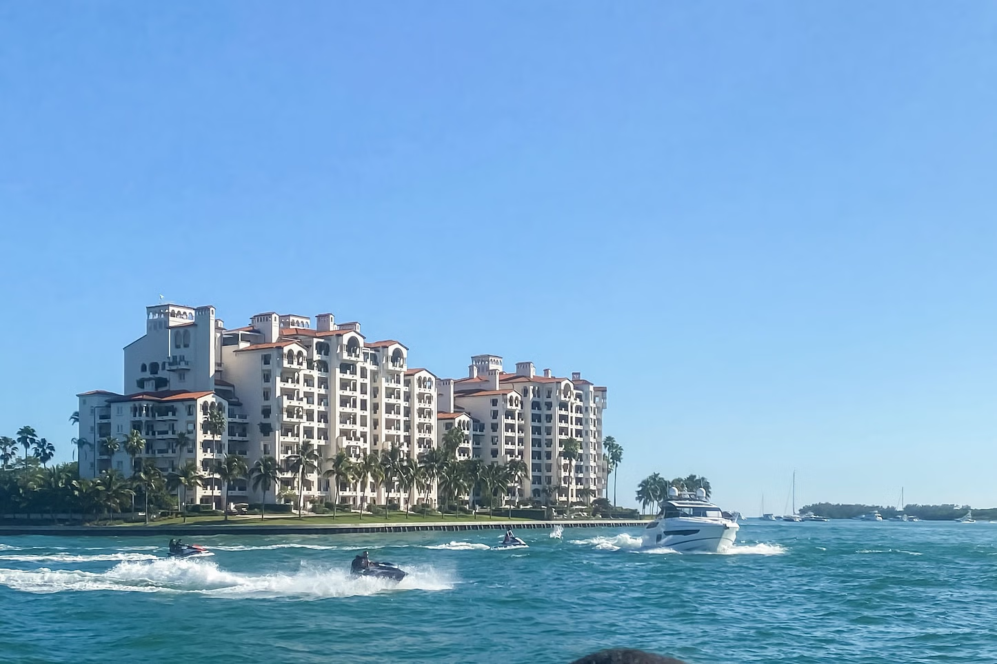 Waterfront luxury condos on a sunny day, with jet skis and a boat in the water.