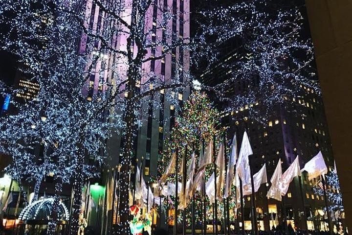 Night view of Rockefeller Center in New York City decorated with Christmas lights and flags.