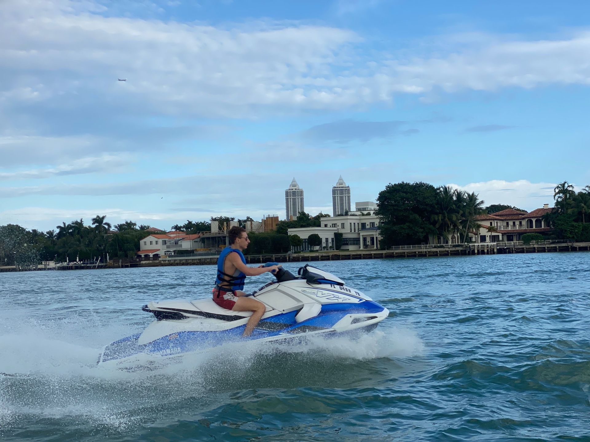 Person riding a blue and white jet ski on a body of water with buildings in the background under a cloudy sky.