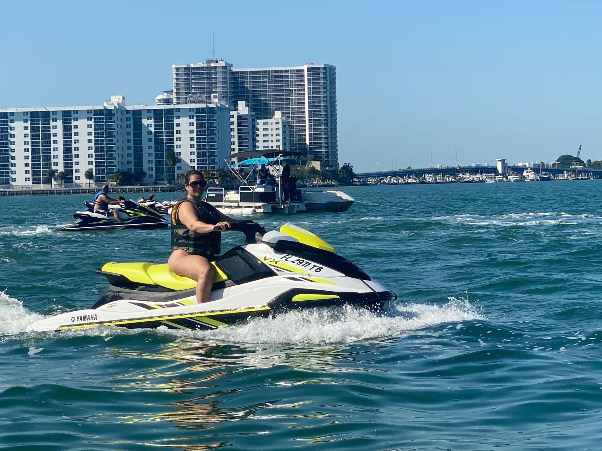 Woman on a yellow and white jet ski in a bay. Skyscrapers and bridge visible in the background.