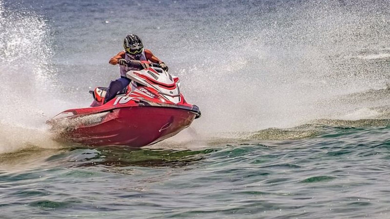 Person on a red jet ski speeding across water, creating splashing white waves.