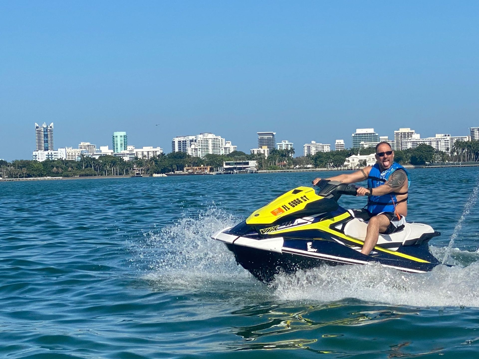 Man on a yellow and blue jet ski on the water with a city skyline in the background.