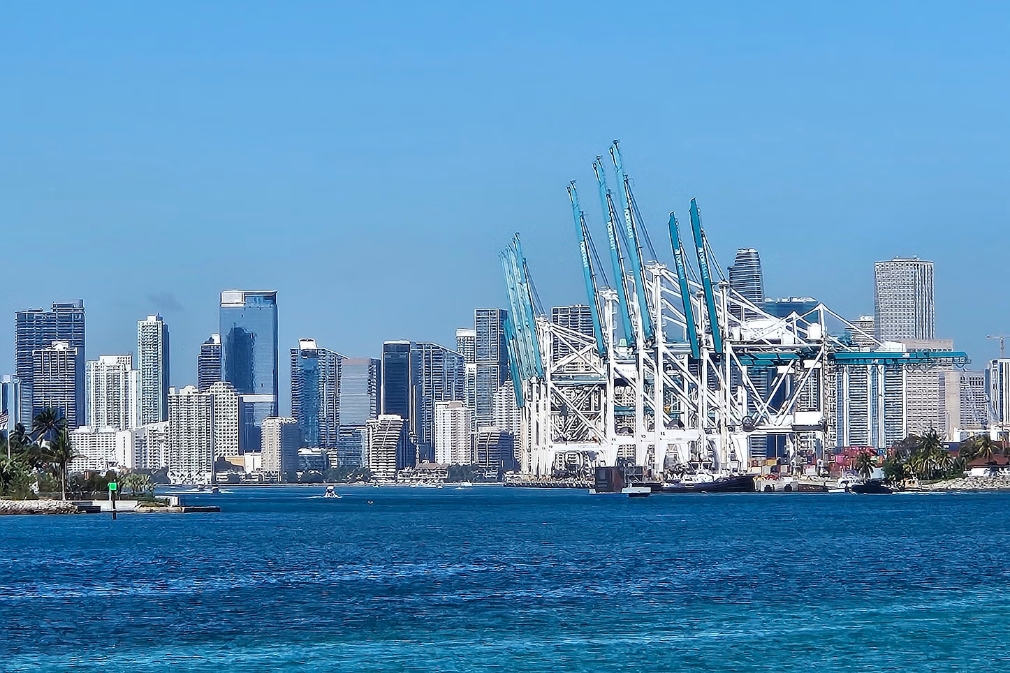 Miami skyline with blue water and white cargo cranes.