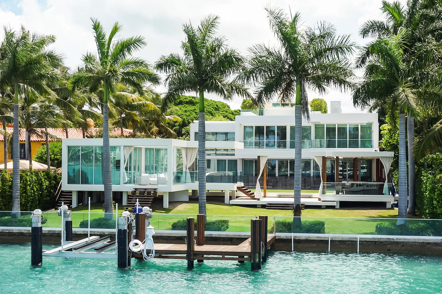 Modern white house on a waterfront with a dock, palm trees, and blue water.