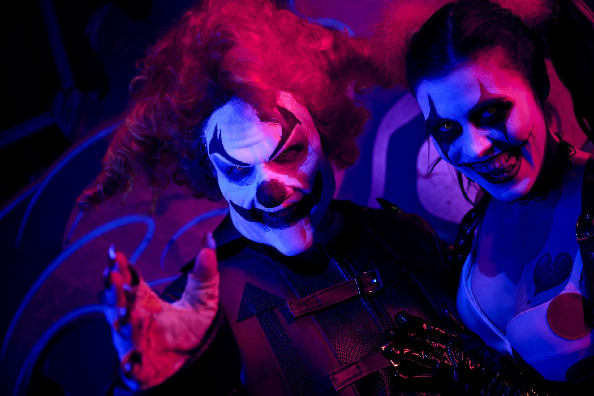 Two clowns with menacing expressions under red and blue stage lighting.