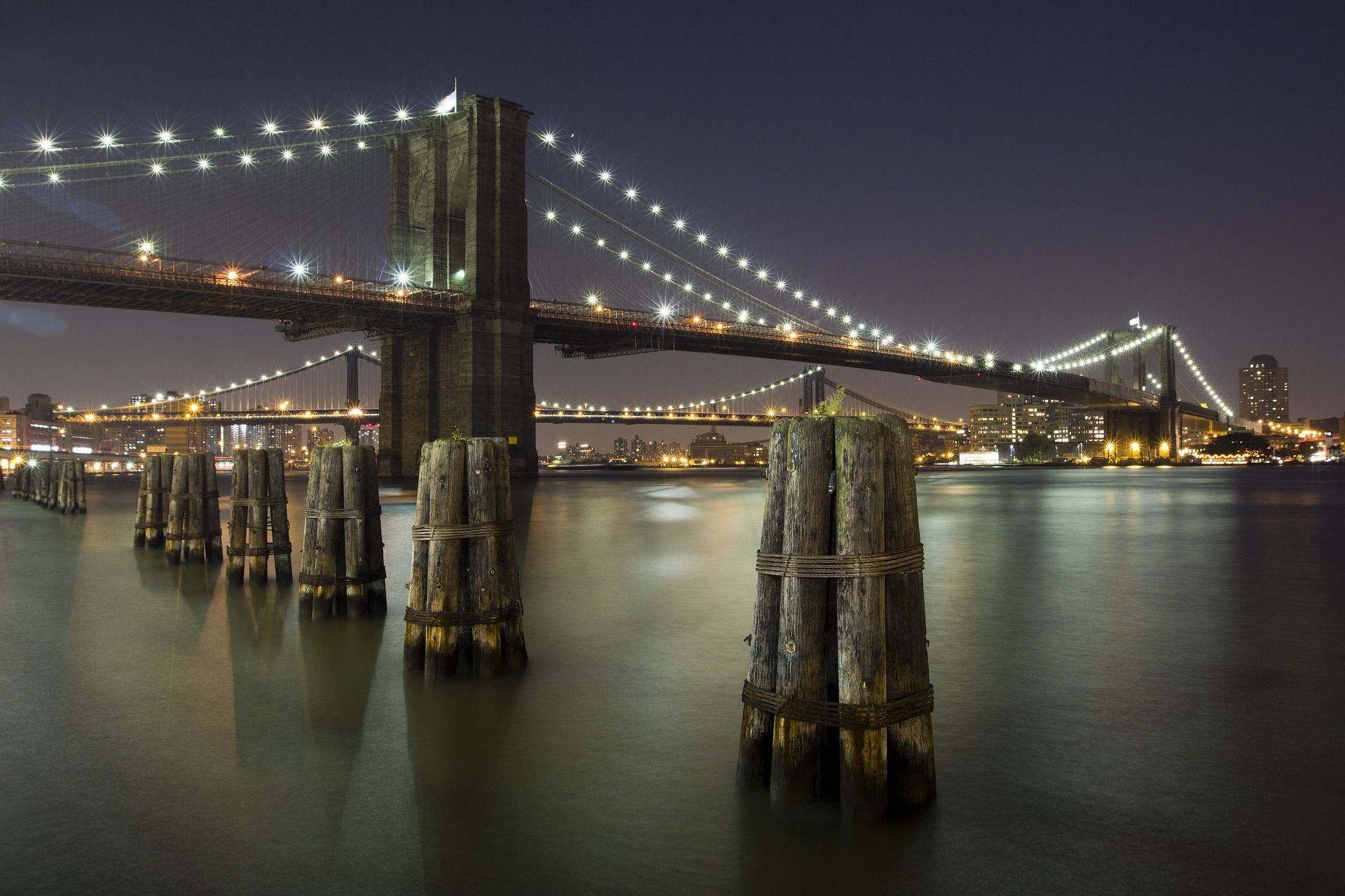 Brooklyn Bridge at night with illuminated lights over water and city skyline.