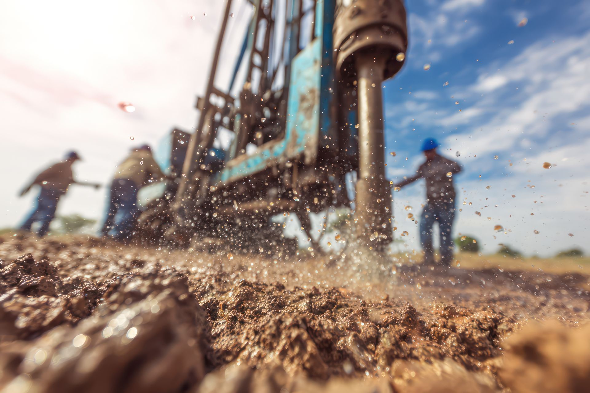 Team of workers with drilling rig on car are drilling artesian well for water in ground. Close-up to the tip of a drilling rig digging a water well with operators in the background.