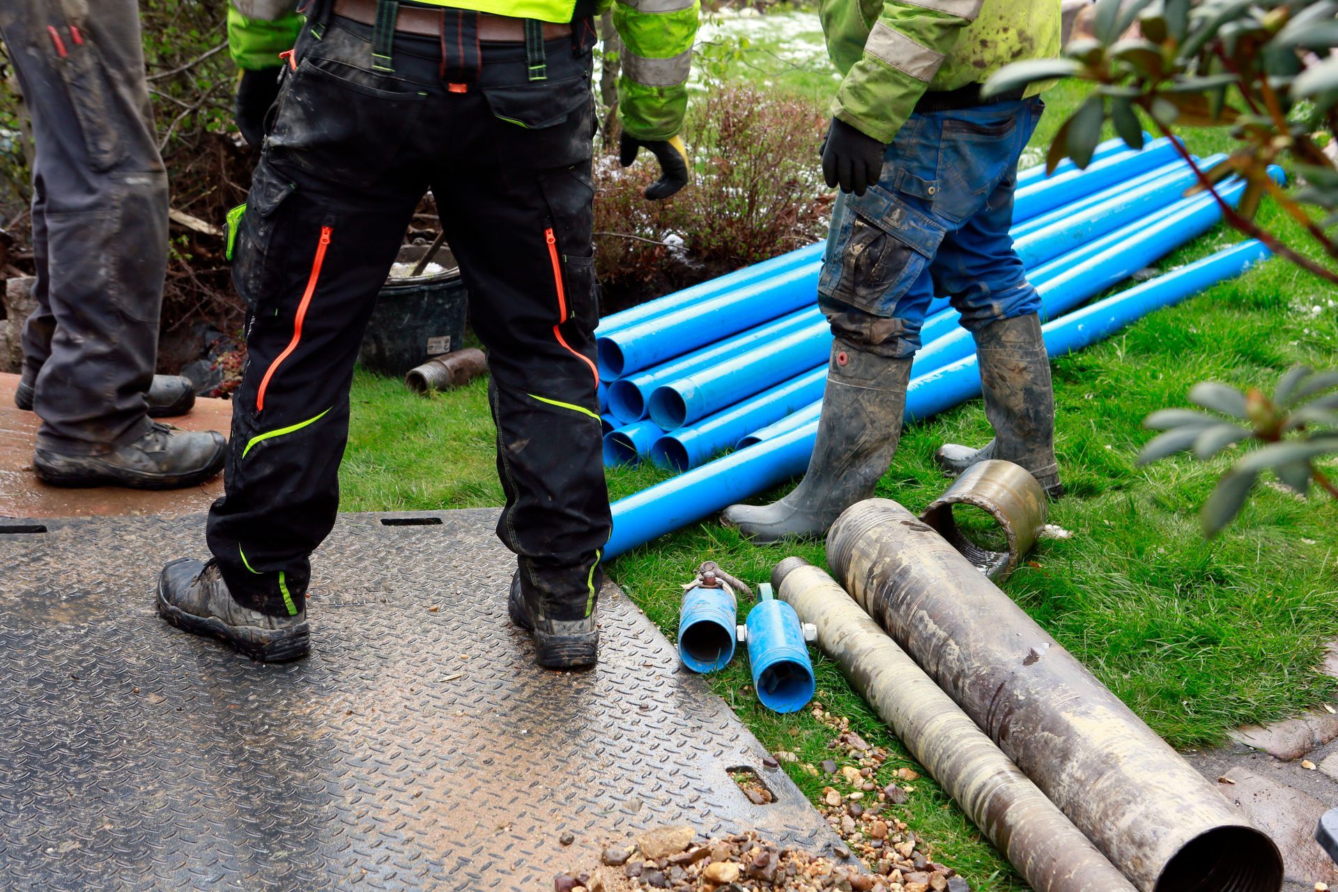 Water pump in action View of the legs of well drilling contractors in a backyard with pipes on the floor.