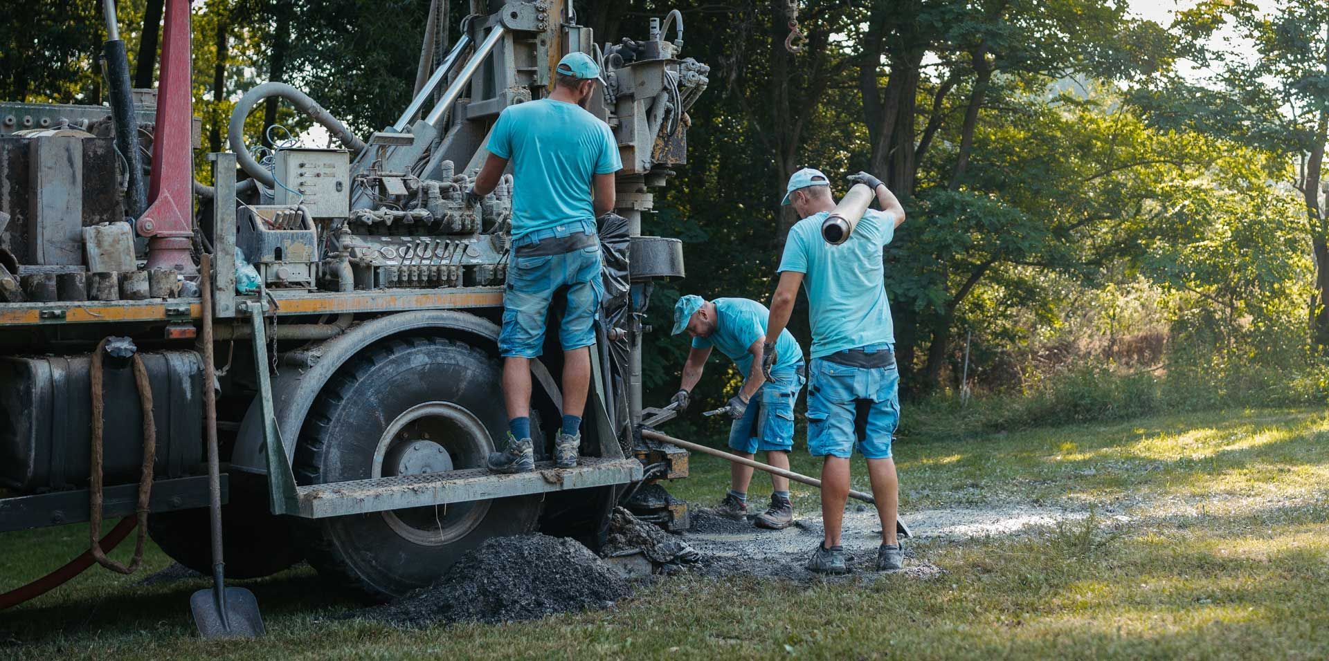 Water well drilling contractor at work, operating machinery and leveling gravel outdoors.
