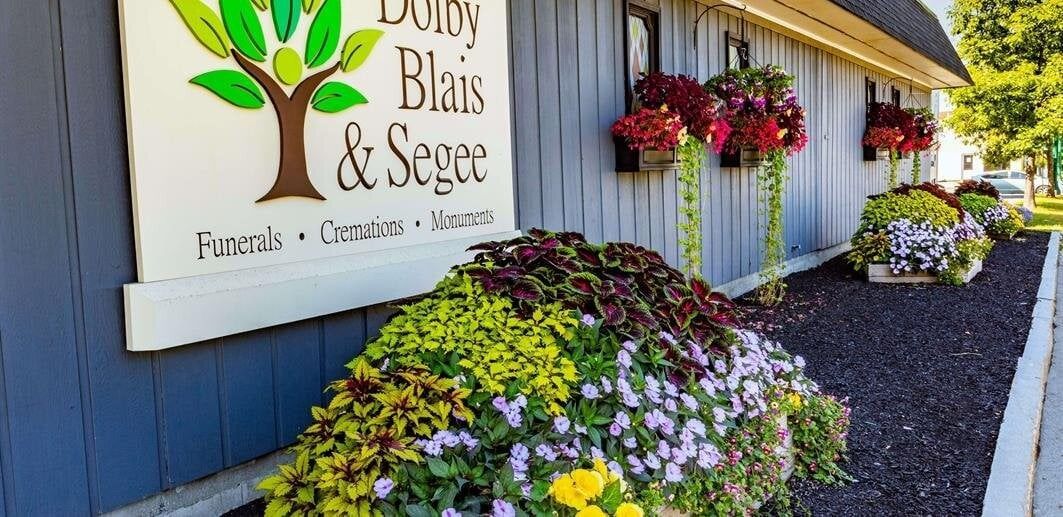 Sign for a shop, "Doris, Blais & Seger", with colorful flowers and hanging baskets.