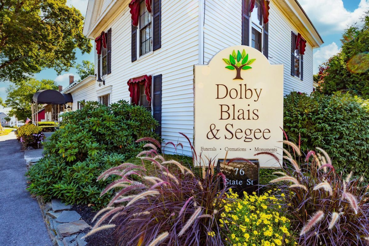 White building with red window coverings, sign for Dolby, Blais & Segee, surrounded by shrubs.