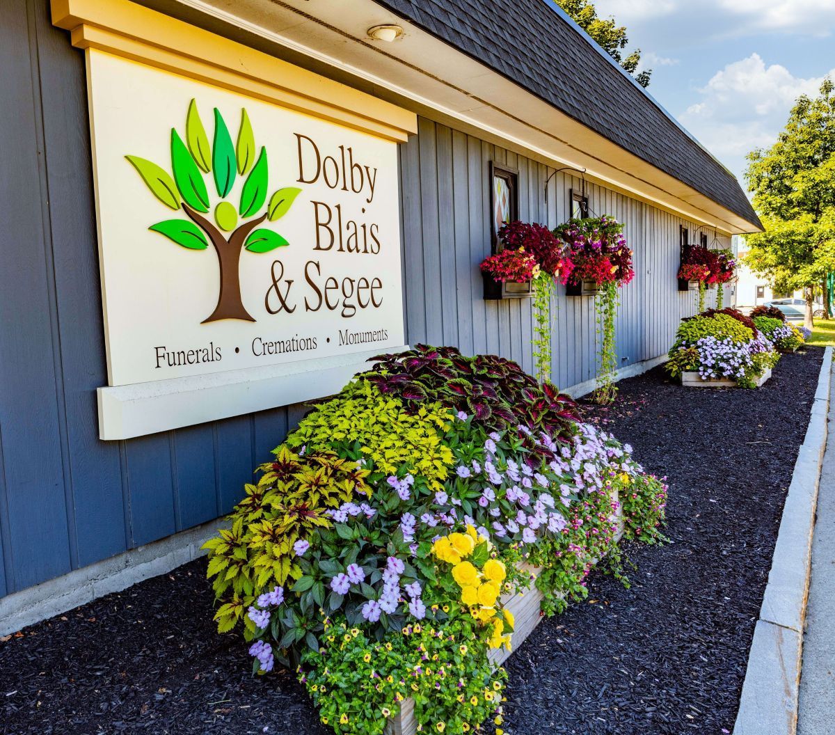 Sign for Dolby, Blais & Segee funeral home with colorful flower beds.