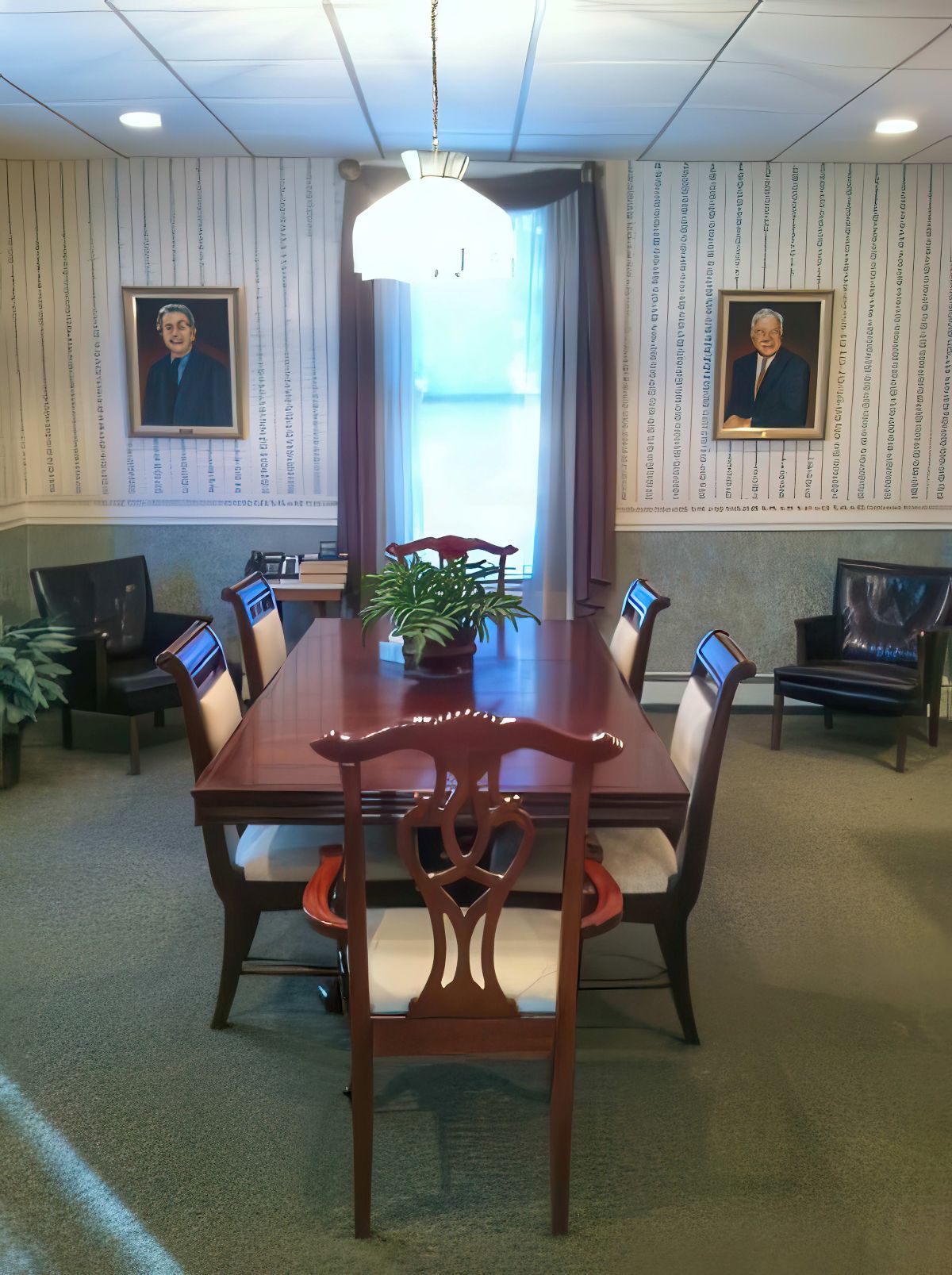 Formal dining room with long table and chairs, portraits on walls, and a window with curtains.