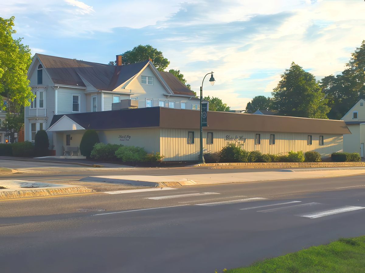 A two-story building and a single-story building sit next to each other on a street with trees and a sidewalk.