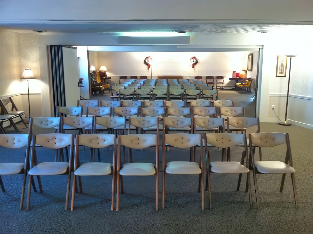 Rows of folding chairs face an open room; interior of a hall, probably for a service.