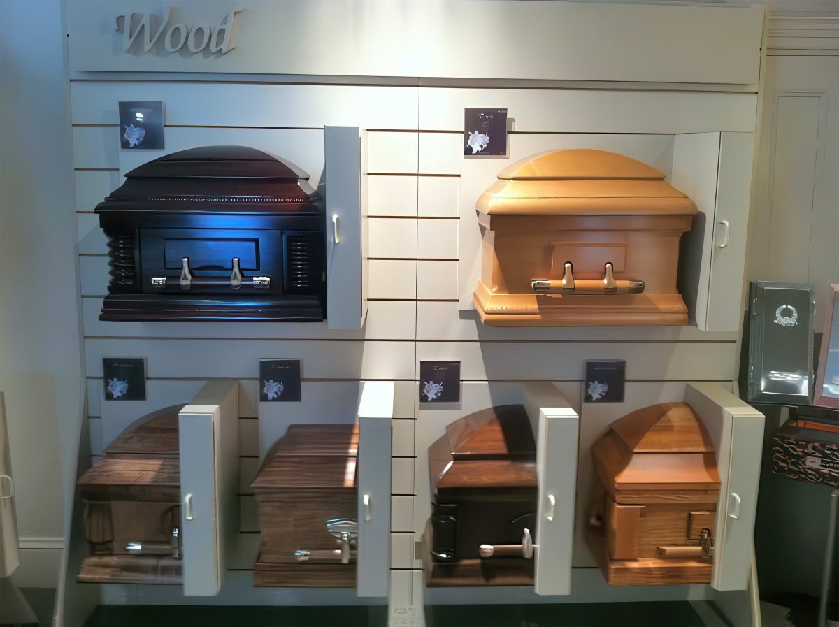Display of wooden caskets in a funeral home. Various shapes and wood tones showcased on a white wall.