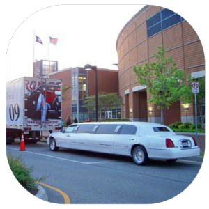White stretch limousine parked on a city street beside a brick arena building.
