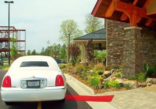 White sedan at a curbside entrance beside a stone building and landscaped garden.